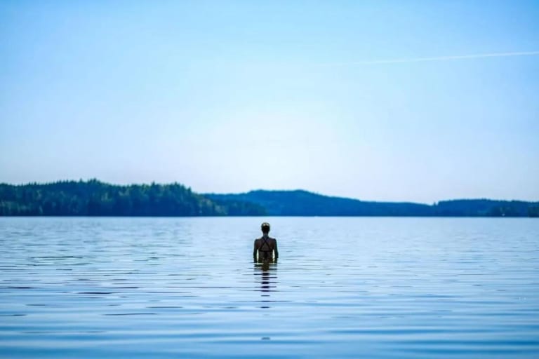 En person badar i en stilla sjö i skymningen.
