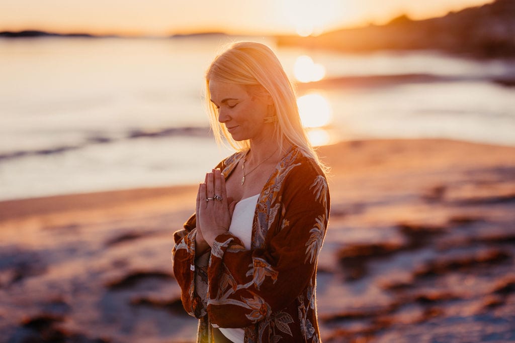 Kvinna med händerna mot hjärtat och slutna ögon vid havet.